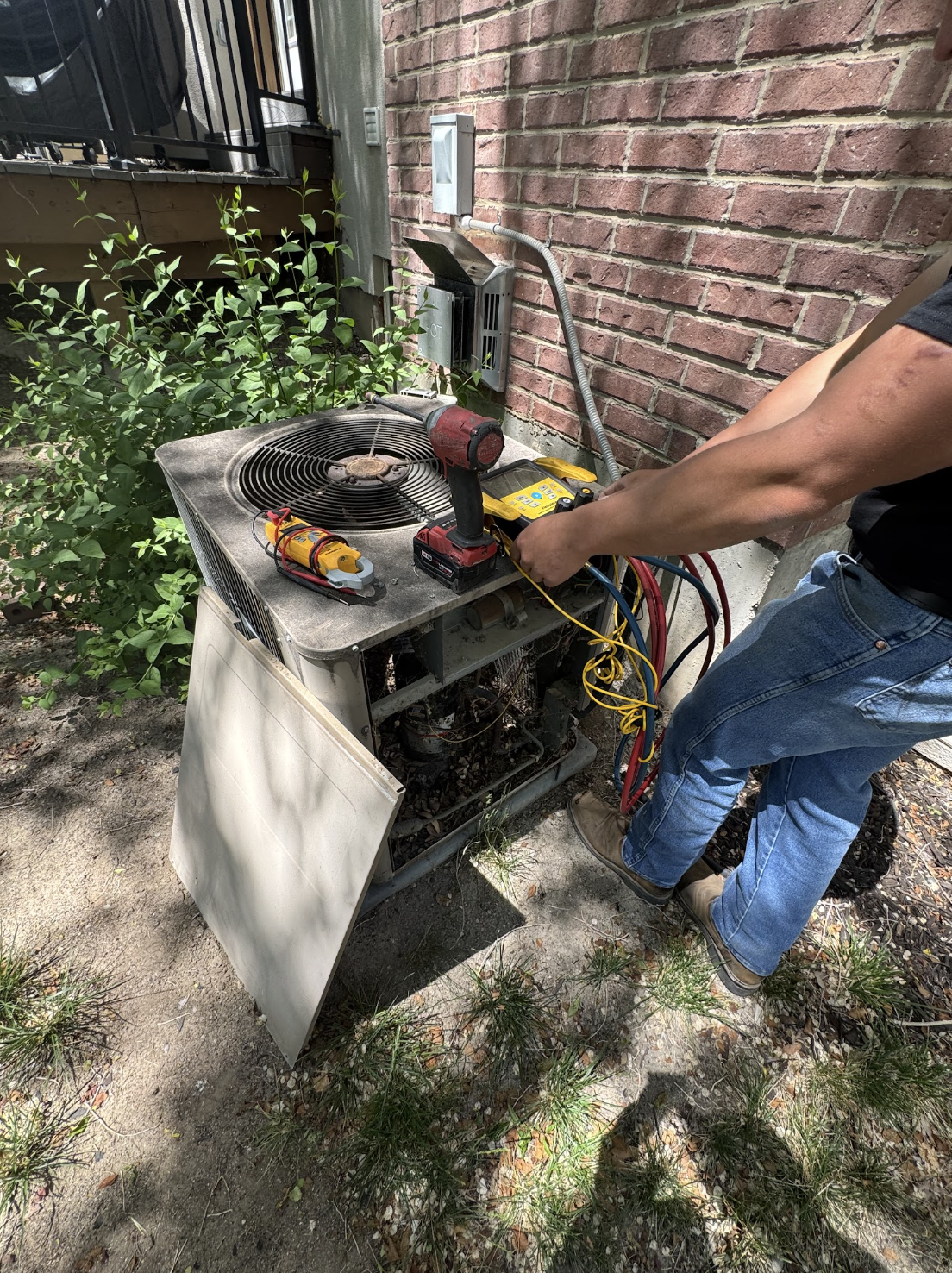 Technician diagnosing an outdoor AC unit with manifold gauges and tools