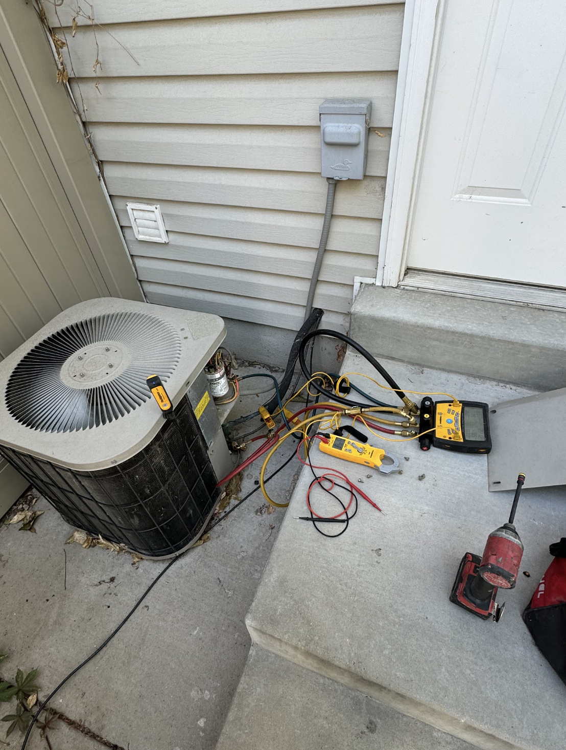 Outdoor AC condenser with manifold gauges and diagnostic tools during service