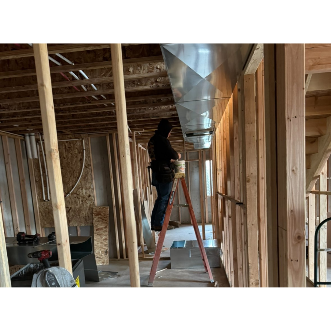Technician installing custom sheet metal ductwork during new construction framing