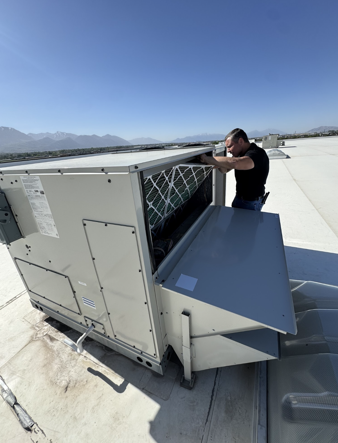 Technician replacing an air filter in a commercial rooftop HVAC unit